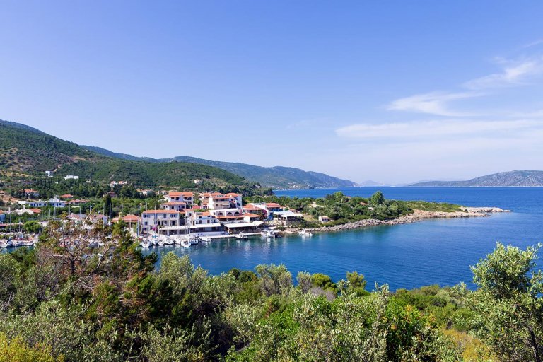 Aerial view of a small harbour village with white houses among green hillside, boats moored along the shore