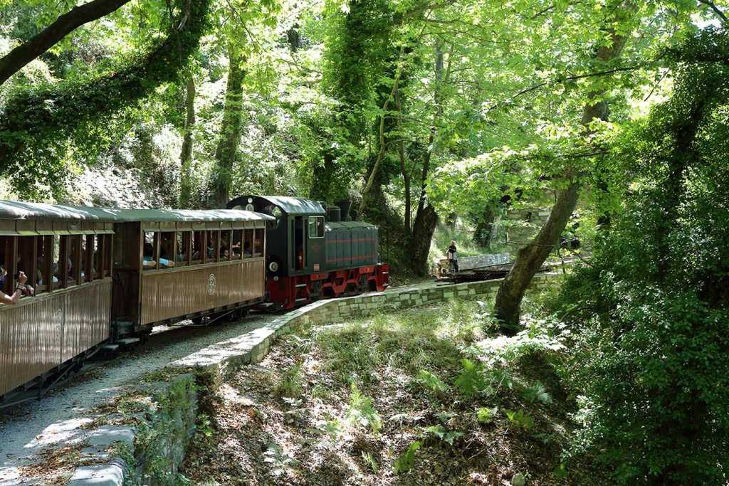 A small steam train with wooden carriages on a curve of the narrow-gauge line through forest