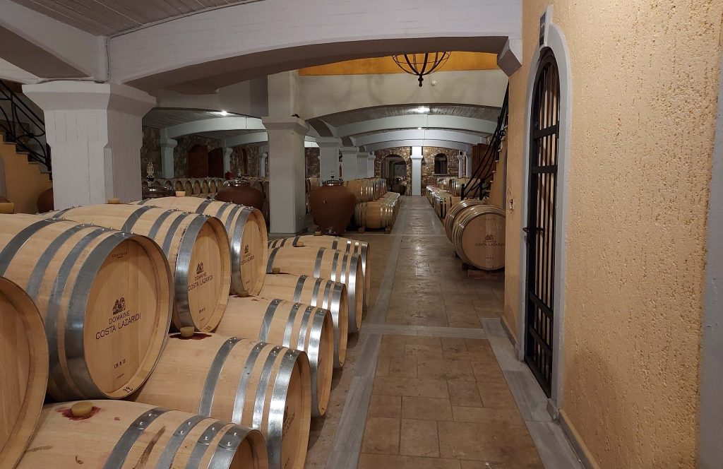 Rows of oak wine barrels along a stone corridor in the cellar of Kostas Lazaridis winery.