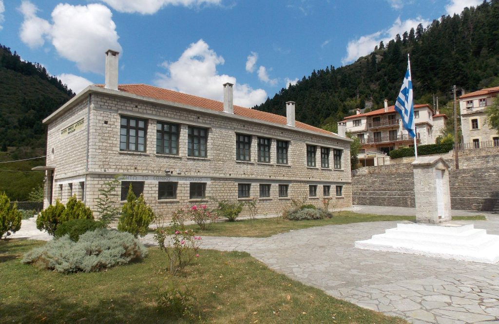 The stone school building in Korischades that houses the Museum of National Resistance, with a Greek flag in front