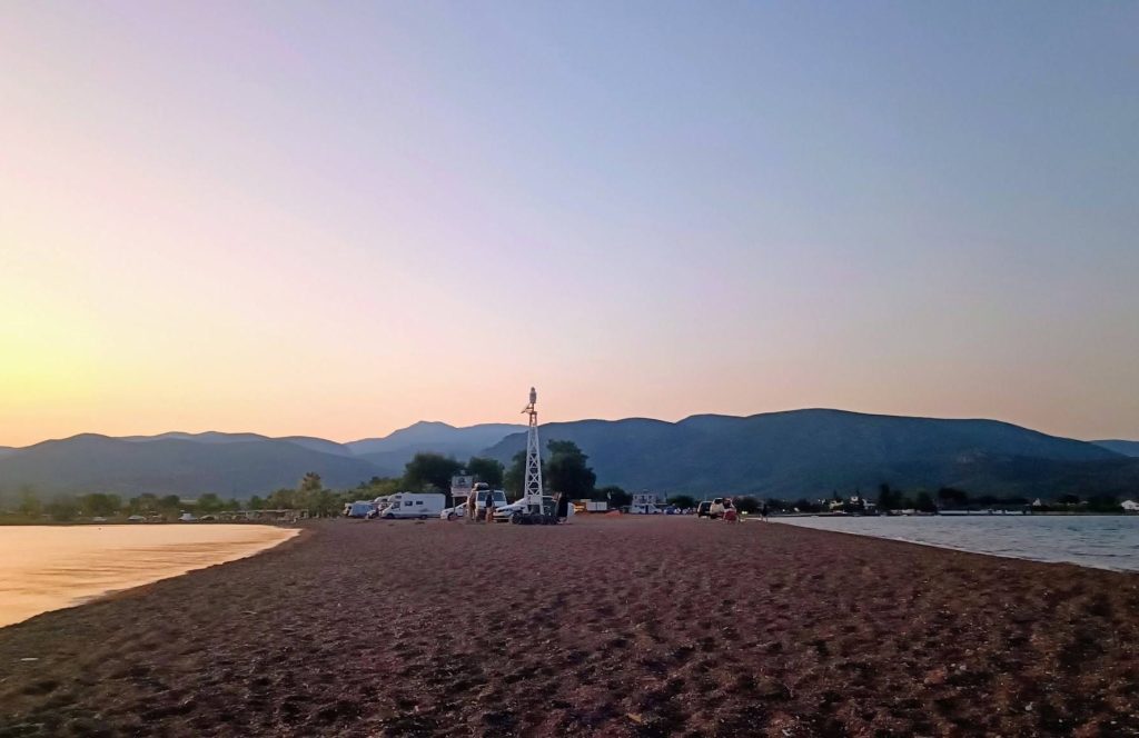 Sand spit of Faros with water on both sides, a small light tower and parked campervans
