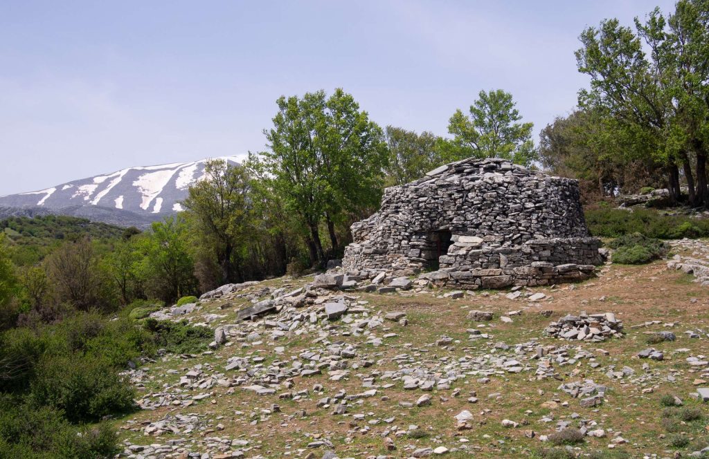 Round dry-stone shepherds' hut on rocky ground, with a snow-covered ridge in the distance