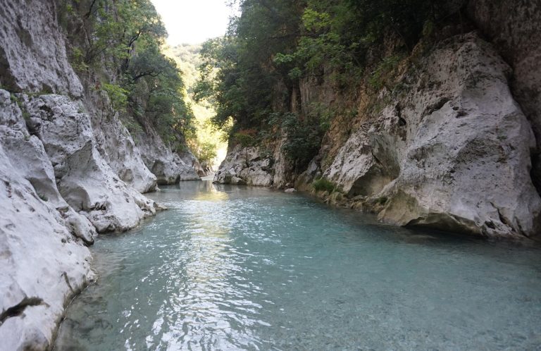 Blue-green river between pale rock walls, with trees above and light at the far end of the gorge