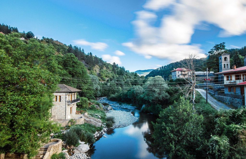 River running between wooded banks below stone houses and a bell tower