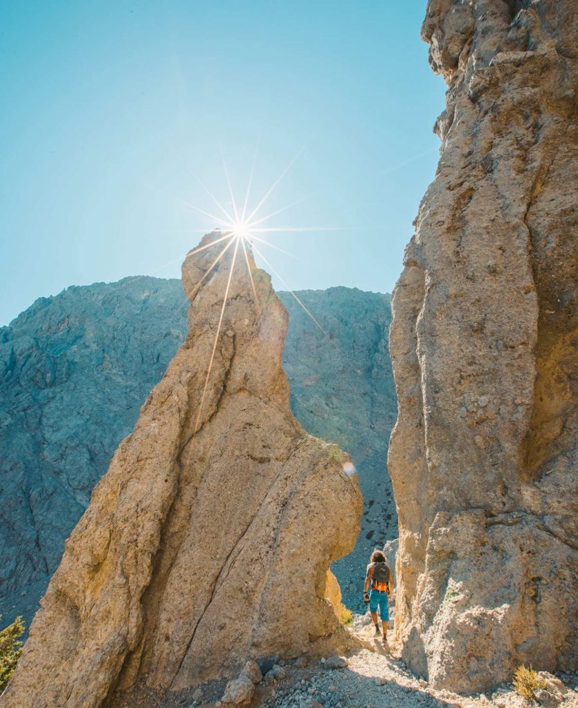 Walker between two tall rock pinnacles, with the sun shining between them