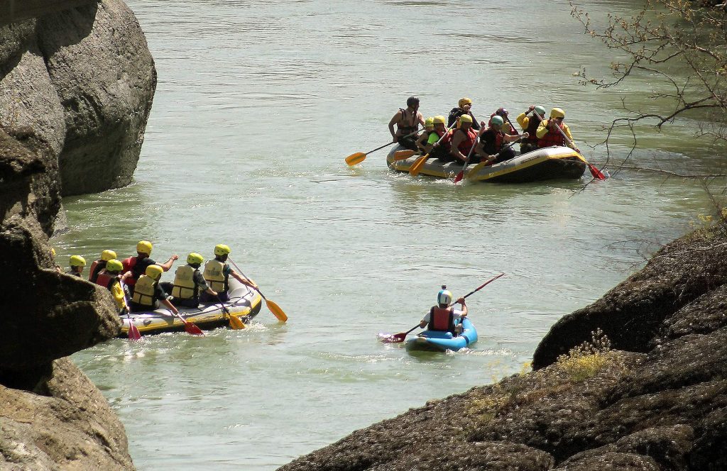 Two rafts and a kayak with paddlers in helmets on a green river between large dark rocks