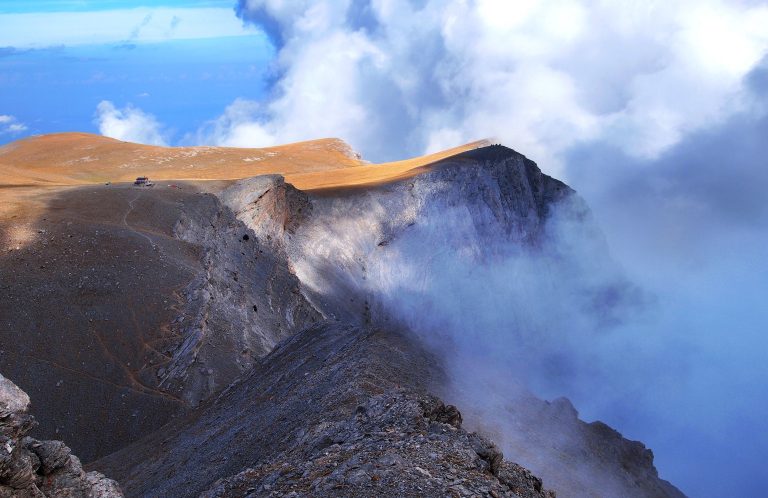 Sheer cliffs dropping into cloud beside a flat sunlit ridge at Drakofolia on Mount Olympus