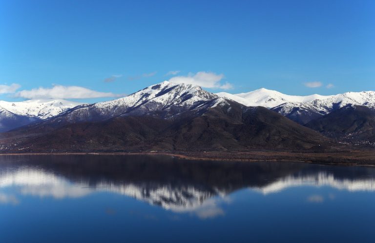 The snow-covered summits of Mount Varnoundas reflected in the still water of Small Prespa Lake