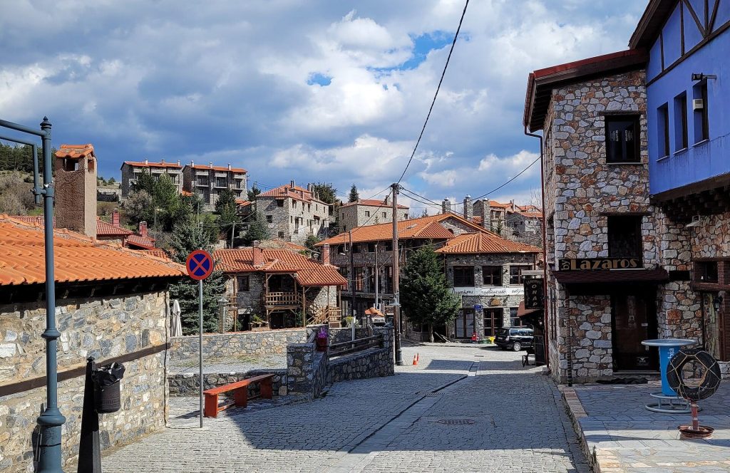 Cobbled street between stone-built houses with red tiled roofs, with more stone houses on the slope behind