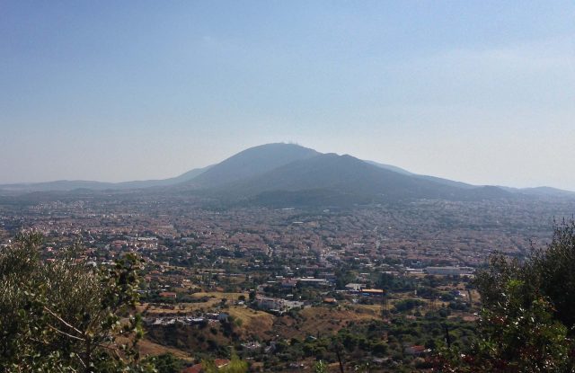 The rounded mass of Mount Penteli rising above a wide built-up plain, seen from a wooded hillside