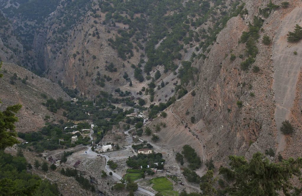 Old stone houses and trees at the bottom of a valley, seen from above