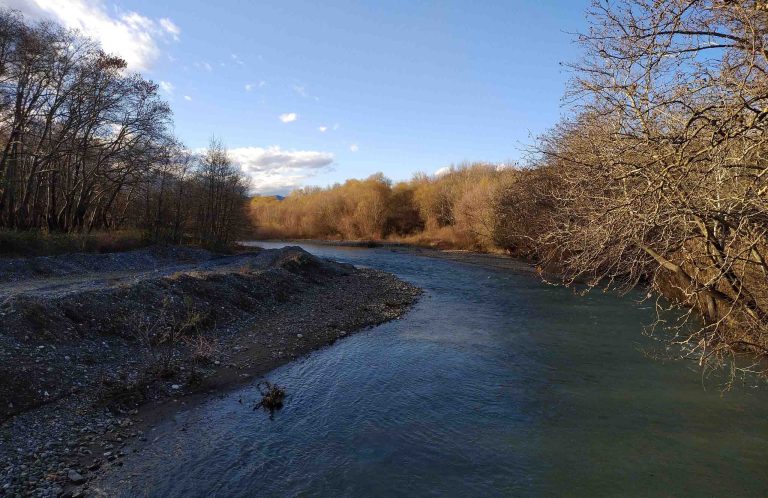 The Sperchios River flowing past a gravel bank, lined with bare and autumn-coloured trees