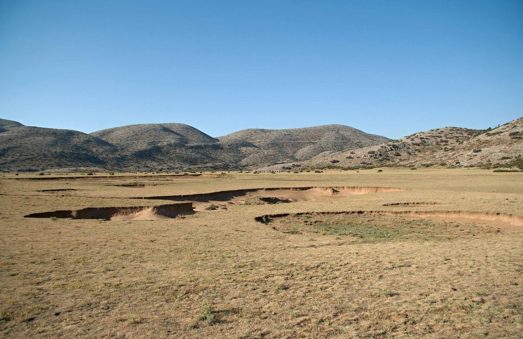 Flat dry grassland of the Nida plateau with sinkholes, closed in by bare hills