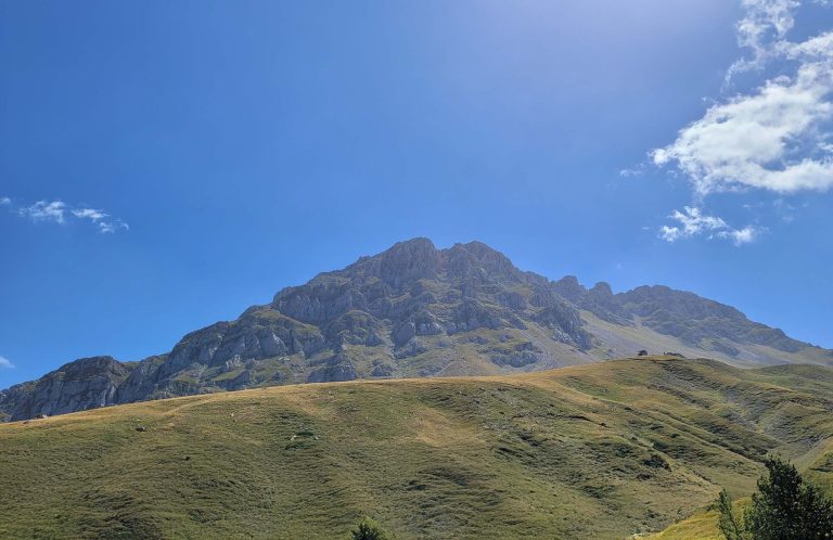 Broad rocky peak rising above grassy slopes under a blue sky