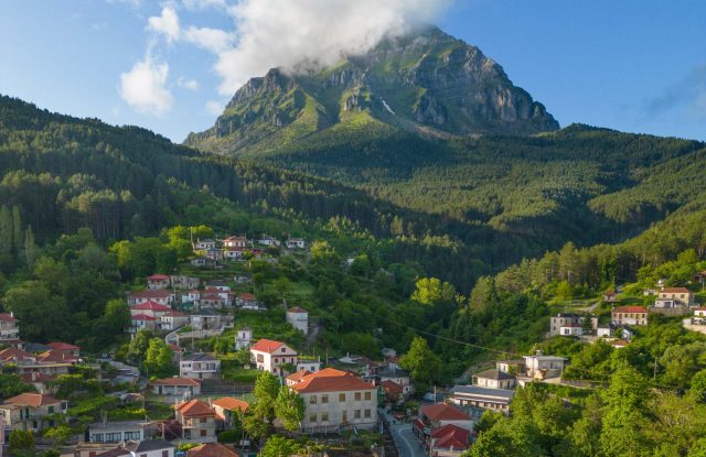 Village with red roofs on a green slope, below a steep rocky peak