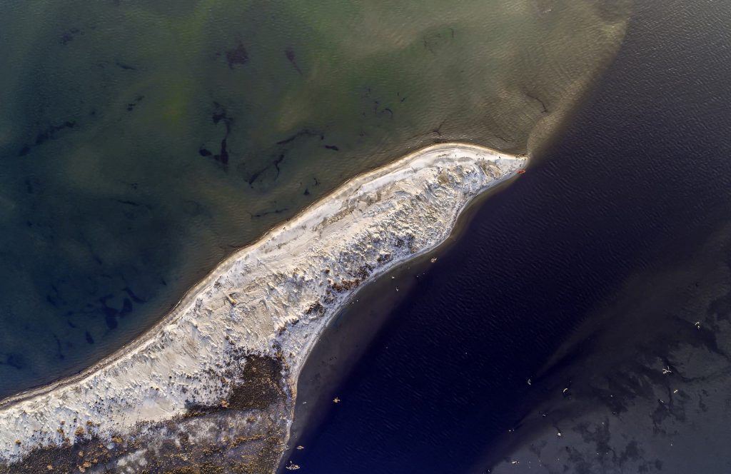 White strip of sand seen from above, between shallow green water and deep dark water