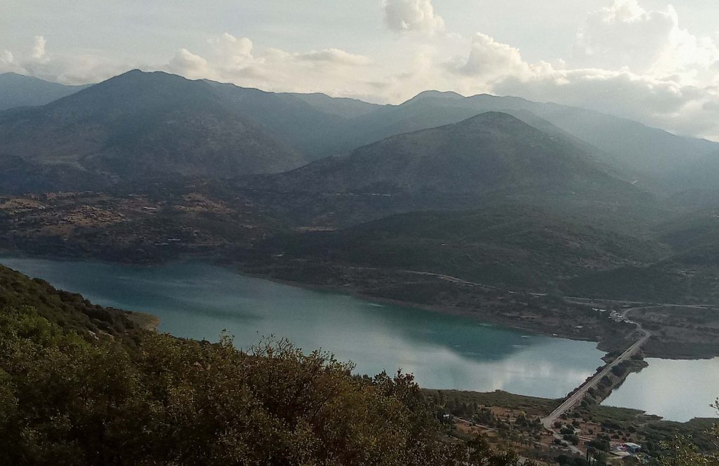 Long arm of a blue-green lake between dark mountain slopes, seen from a hill