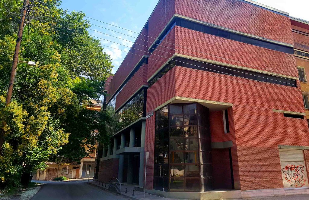 Modern red-brick building of the Drama library, with large glass windows and trees in front.