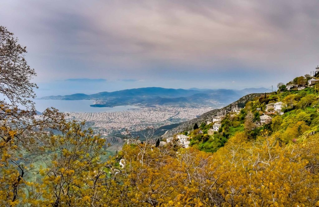 View over autumn-coloured trees and a hillside village to the city of Volos and the Pagasetic Gulf